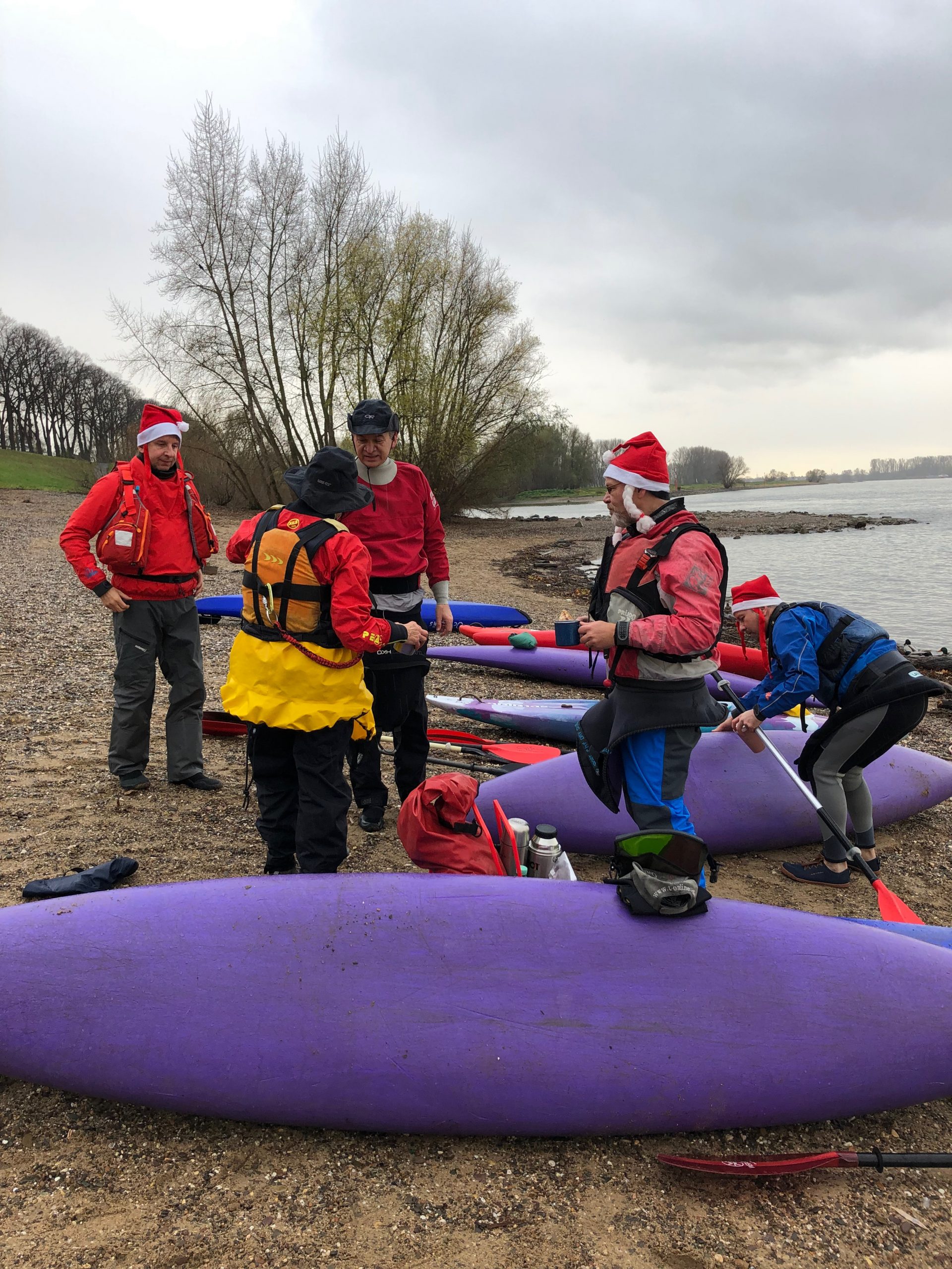 Mehrere Kanufahrer mit Nikolausmützen am Rhein mit Glühwein